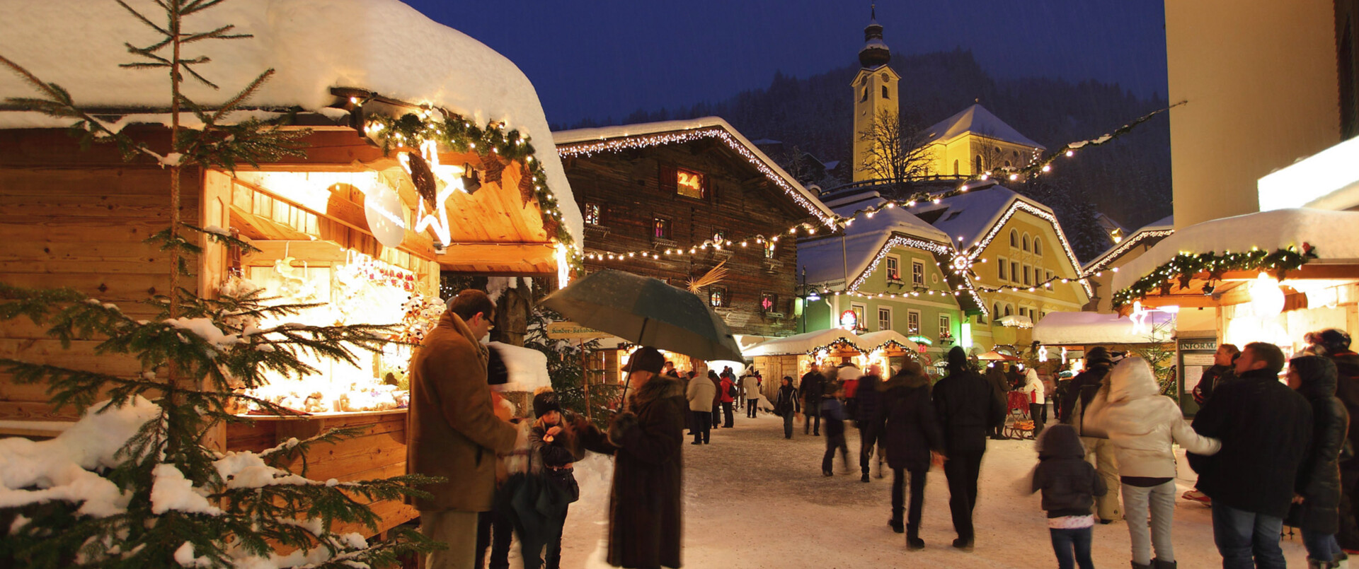 Blick auf den tiefverschneiten Dorfplatz und den weihnachtlich geschmückten Hütten beim Adventmarkt in Großarl.