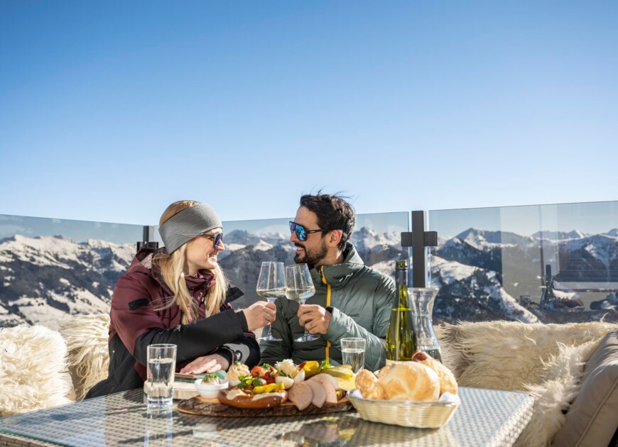 Ein Paar prostet sich mit einem Glas Wein auf der Sonnenterrasse auf einer Hütte am Berg in Großarl zu.